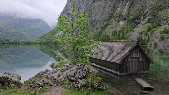 Crystal-clear waters of Lake Obersee reflect a rustic wooden boathouse and lush alpine meadows in Berchtesgaden National Park, surrounded by dramatic mountain cliffs