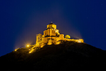 Obraz premium Night view of Jvari Monastery. Stone walls are illuminated with warm light. Traces of spotlights are visible. Dark blue sky with stars in the background
