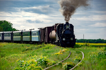Steam locomotive on the move. Narrow gauge railway.The locomotive smokes, giving a signal. Weekend tour. Tourism Ukraine. Picturesque route.
