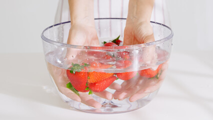 A pair of hands gently hold strawberries under water in a transparent bowl during