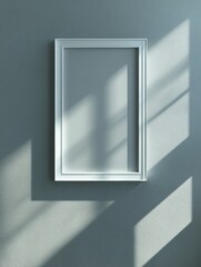 Empty white frame on a muted gray wall, illuminated by sunlight.