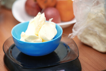Pieces of butter in a blue ceramic bowl being weighed on digital kitchen scales for precise baking measurements