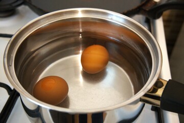 Two brown chicken eggs in water in cooking pot.