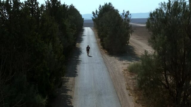 Aerial: Drone Forward Shot Of Man Walking Alone On Road During Sunny Day - Tel Arad, Israel