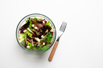Top view of a green salad with pomegranate and cheese, and a fork, on light background with copy space.
