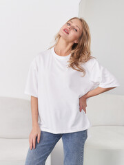 Smiling woman with long hair wearing a white oversized T-shirt and blue jeans, standing confidently...