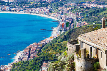 Aerial view of coastline in eastern Sicily between Taormina and Giardini Naxos. Traditional Sicilian architecture, turquoise waters of Mediterranean Sea, and lush Mediterranean vegetation 