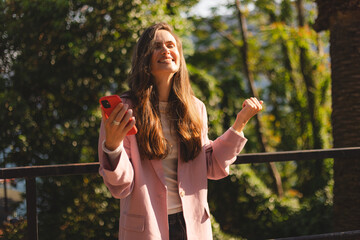 Business woman, phone and celebrate outdoor for success, achievement or win. Excited brunette long hair female entrepreneur with a smartphone on sidewalk for online competition or bank notification.