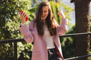 Business woman, phone and celebrate outdoor for success, achievement or win. Excited brunette long hair female entrepreneur with a smartphone on sidewalk for online competition or bank notification.