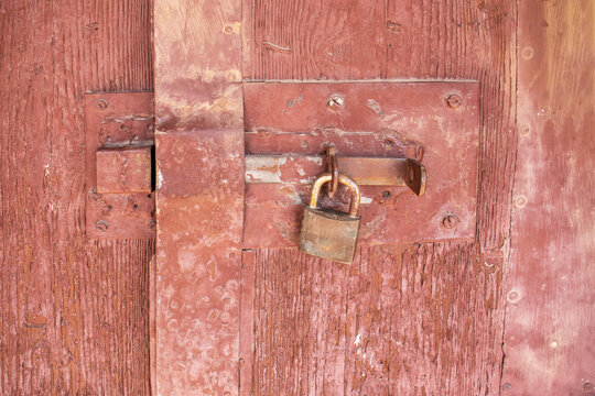Close-up of an old rusty padlock securing a weathered wooden door with a metal latch