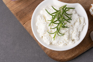 Creamy cottage cheese with fresh rosemary on a wooden tabletop
