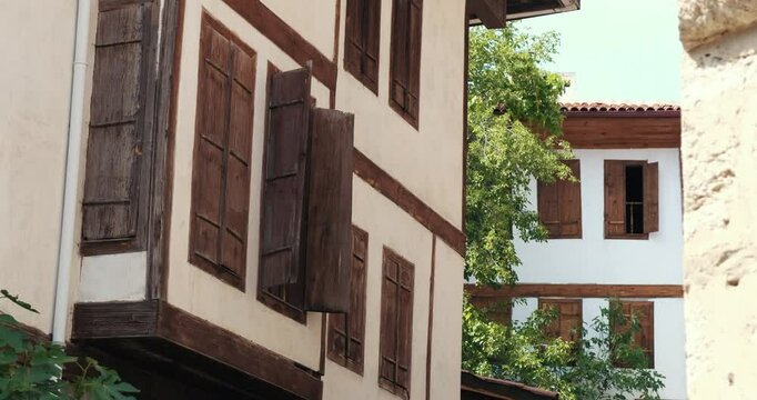 The architecture of traditional Turkish houses in Safranbolu is seen. Ottoman-era houses with wooden details, bay-windowed structures and brown shutters. An open window sash is in the foreground.