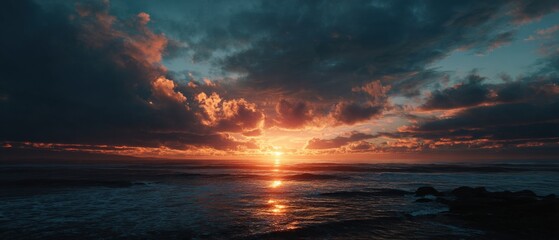Fiery sunset over the ocean, casting warm hues across the dramatic cloudscape.