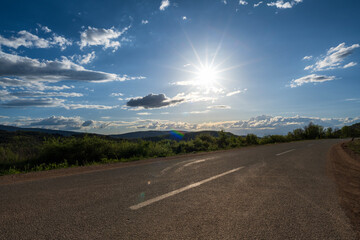 An empty highway passing through the mountains. Beautiful sunset with white clouds and blue sky.

