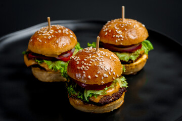 Three juicy mini cheeseburgers on a black background. 