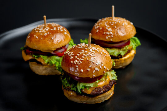 Three juicy mini cheeseburgers on a black background. 