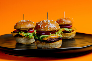 Three mini cheeseburgers on a vibrant background. 