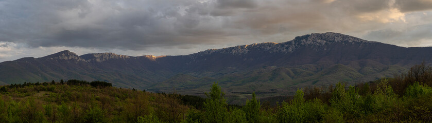 Obraz premium Mountain peaks in the woods landscape. Panoramic view of Suva Plnina mountain range in Serbia. Panoramic photo. Panorama of the mountain range. Sunset and beautiful clouds cover the mountain range. 