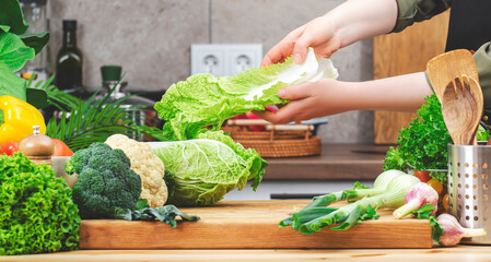 Chef cooking food in the kitchen. Cook hands holds Chinese cabbage. Wooden table, kitchenware, vegetables, herbs and ingredients. Healthy vegan eating, recipes, blogging