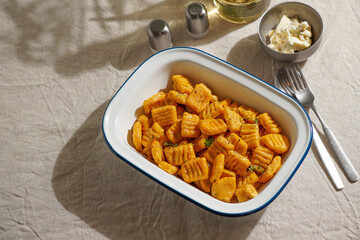 pumpkin gnocchi, garnished with fresh herbs in Enamel Bowl with Cutlery on Linen Tablecloth