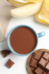 Tasty chocolate milk in cup, pieces and banana on white wooden table, flat lay