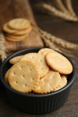Tasty salty crackers and wheat spikes on wooden table, closeup