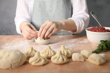 Woman making khinkali on table in kitchen, closeup