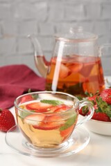 Aromatic fruit tea with strawberries and mint on white table, closeup