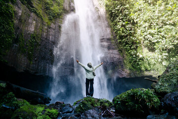 Hijabi Woman Embracing Nature Under Tall Waterfall