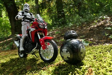Naklejka premium Star Wars articulated action figure of Clone Trooper riding on dual sport japanese motorbike Honda Africa Twin, chasing black ball shaped imperial droid BB-9E.