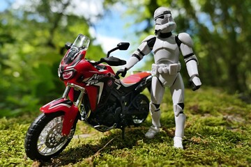Naklejka premium Star Wars articulated action figure of Clone Trooper examining model of dual sport japanese motorbike Honda Africa Twin parked on mossy landscape in spring forest. 