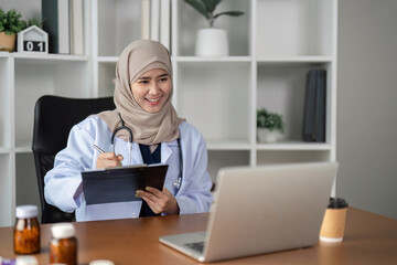 Smiling female doctor in hijab conducting a virtual consultation with a patient using a laptop.