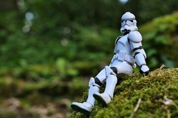 Naklejka premium Star Wars articulated action figure of Clone Trooper soldier in white armor, sitting relaxed on mossy stone in shadow of spring foliage. 