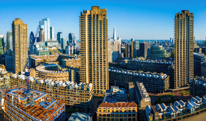Colorful aerial view of London's Barbican Estate with high-rise buildings, modern architecture, and city skyline under a blue sky © Alexey Fedorenko