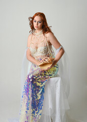 Fantasy studio portrait of a red-haired mermaid faery model wearing white pearl gown, fairytale...