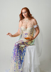 Fantasy studio portrait of a red-haired mermaid faery model wearing white pearl gown, fairytale...