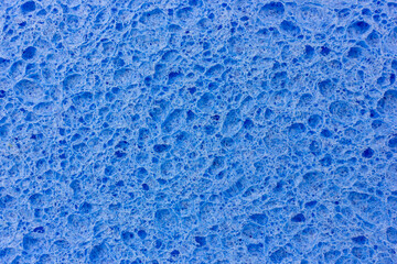 A close-up shot reveals the intricate, porous texture of a light blue cleaning sponge