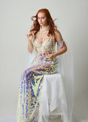 Fantasy studio portrait of a red-haired mermaid faery model wearing white pearl gown, fairytale...