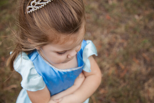 Little girl in princess dress ups costume and tiara looking down