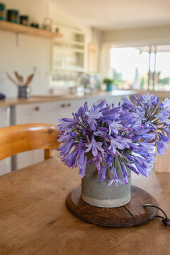 flowers in a vase on a timber dining table, kitchen in background