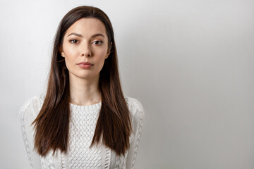Close-up of a calm, serious, emotionless young woman with brown hair, isolated on a white background.