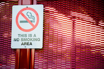 This is a no smoking area sign on red bus stop shelter
