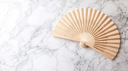 Light beige bamboo hand fan rests on a white marble surface.