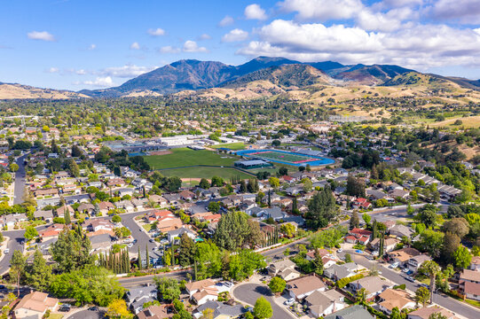 Aerial drone view of Concord, California, featuring residential neighborhoods, a sports complex, and Mount Diablo in the scenic background under a partly cloudy blue sky.