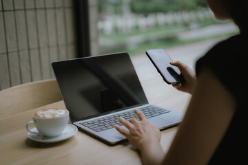 Businesswoman using smartphone on laptop screen in coffee shop