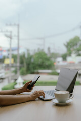 Businesswoman using smartphone on laptop screen in coffee shop