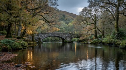 Fototapeta premium Scenic Overview of a Stone Arch Bridge Reflecting in a Serene River Surrounded by Autumn Foliage and Misty Mountains