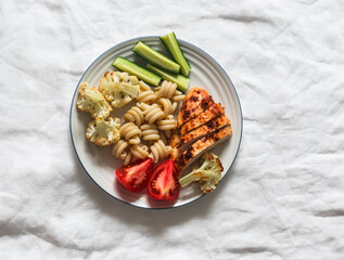 Delicious balanced lunch - grilled chicken breast, pasta, baked cauliflower, fresh vegetables on a light background, top view