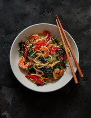 Asian style food - egg noodles with shrimp, sweet pepper and spinach on a dark background, top view