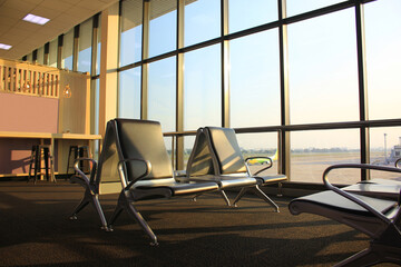 Empty chairs and passenger in the airport terminal on evening sunset light